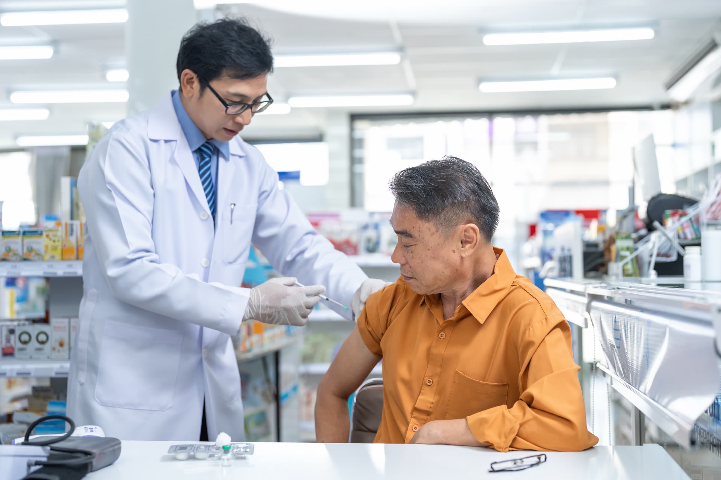 A pharmacist administering a vaccine to an older adult at a pharmacy table